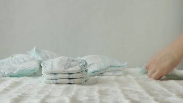 Mother collects a stack of baby diapers on a white background, copy space, hygienics