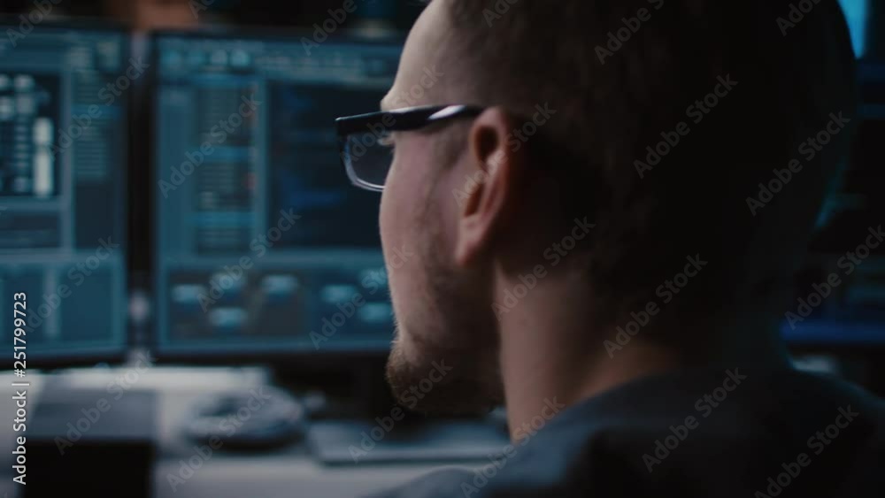 Fototapete Portrait of IT Specialist Wearing Glasses Works on Personal Computer with Screens Showing Software Program with Coding Language Interface. Dark Colors. Close-up Moving Shot