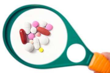 pills under a magnifying glass on the white background. Testing, verification and determining pharmaceutical counterfeiting or fake