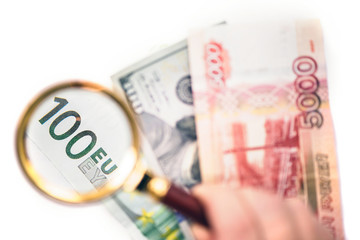 Hundred euro under a magnifying glass on the bacdrop dollar and ruble banknotes. Сoncept of the main international currency