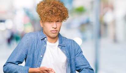 Young handsome man with afro hair wearing denim jacket In hurry pointing to watch time, impatience,...