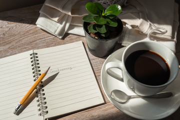 coffee cup, pencil and notebook on wooden in the morning light.