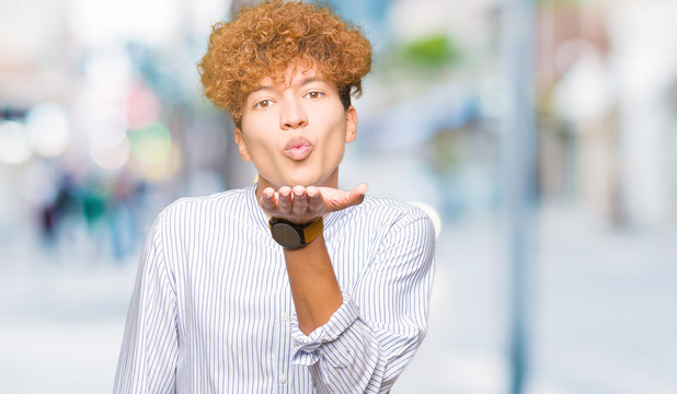 Young handsome business man with afro hair wearing elegant shirt looking at the camera blowing a kiss with hand on air being lovely and sexy. Love expression.