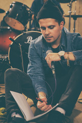 Concentrated singer sitting on floor, holding microphone in hand. Musician looking down at papers,...