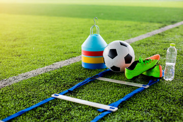ladder drills, goal, soccer ball, marker cones, sports shoes and bottle water on green artificial...