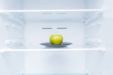 One green apple in open empty refrigerator. Weight loss diet concept.