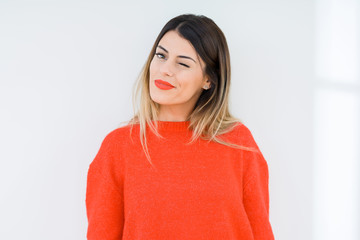 Young woman wearing casual red sweater over isolated background winking looking at the camera with...