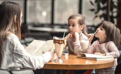 Happy young women mother with children sitting at dinner table and talking in restaurant