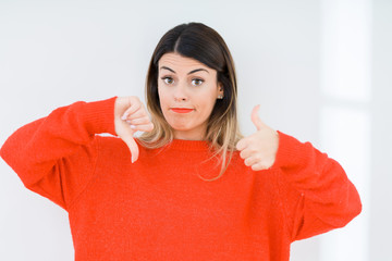 Young woman wearing casual red sweater over isolated background Doing thumbs up and down, disagreement and agreement expression. Crazy conflict