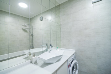 Modern bathroom with a shower area and bath tub including a wall mirror near a tap and sink over the counter and cupboard