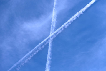 A background of blue sky with white clouds and white intersections of the lines of the trail of overflying airplanes. Background, cropped shot, horizontal, outdoors, nobody. Ecology concept.