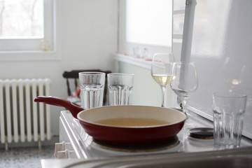 Obraz na płótnie Canvas part of the kitchen and dishes after intimate lunch or dinner for two with white wine. Glass for water, wine and red pan at kitchen range 
