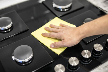 Young man hands in rubber protective cleaning and polish cooker. Black shiny surface of kitchen top, hands, detergent. Set cleaning concept