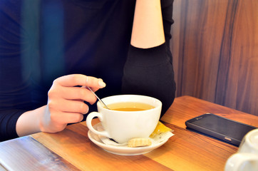 A young girl in a caf&eacute; is drinking tea while checking the messages on the phone. a woman on a pause for drinking tea