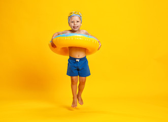 happy child boy in swimsuit with swimming ring donut on colored yellow background