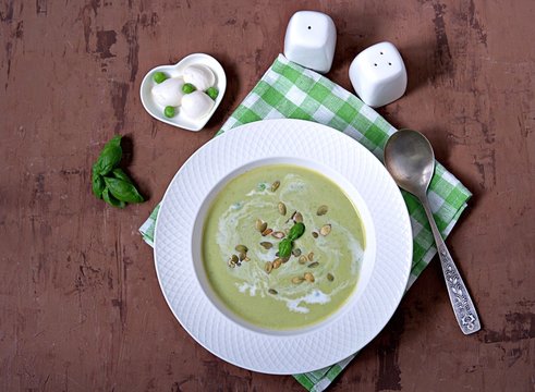 Cream of green pea soup, sprinkled with pumpkin seeds, in a white plate. Served with mozzarella cheese.