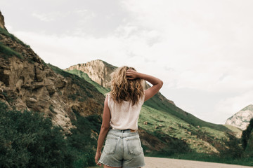 Naklejka premium fashionable girl in white clothes standing on the road in the highlands . green grass and mountains