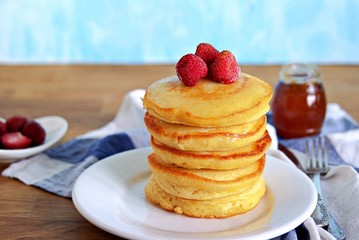 Cornmeal pancakes on a white plate. Served with frozen strawberries and honey or maple syrup.