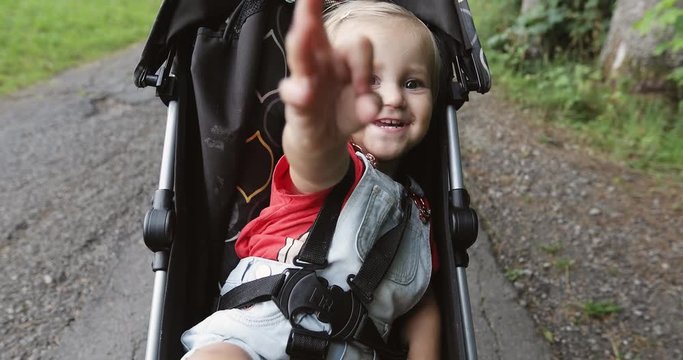 Happy little girl sitting in a baby carriage in summer.
