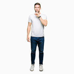 Handsome man wearing casual white t-shirt asking to be quiet with finger on lips. Silence and...