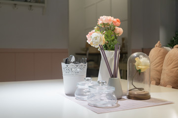 Still life of dining room. Close up of dining table decorated with rose flowers in small glass and vase with kitchen on background.