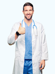 Handsome doctor man wearing medical uniform over isolated background doing happy thumbs up gesture with hand. Approving expression looking at the camera showing success.