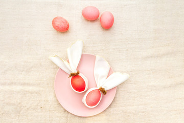 Easter bunny (rabbit) egg concept, table arrangement decoration. Pink (rosy) eggs with plate on cloth vintage linen napkin (canvas) background, top view