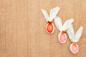 Easter bunny (rabbit) egg concept, table arrangement decoration. Pink (rosy) eggs with napkins on cloth (linen) background, top view