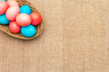 Easter eggs concept, table arrangement decoration. Pink (rosy) and blue eggs in wicker basket on cloth (linen) background, top view