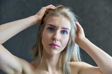 Closeup portrait concept of a beautiful blonde girl on a gray background. Hair develops in different directions.