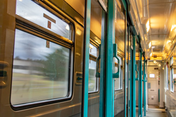 Fototapeta premium The corridor of wagon with reflection of surroundings in door glass. The interior of moving train with long corridor and doors and windows.