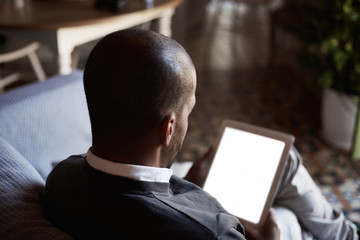 African black man using tablet on sofa couch in home living room