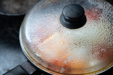 Hot pan with food covered with a glass lid that sweats up