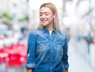 Young blonde woman over isolated background looking away to side with smile on face, natural expression. Laughing confident.