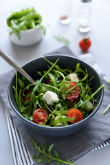 Bowl of arugula salad with tomatoes and cheese on gray wooden background. Vegetarian food concept