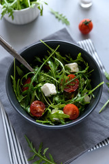 Bowl of arugula salad with tomatoes and cheese on gray wooden background. Vegetarian food concept