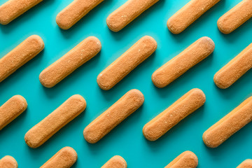 Pattern of sponge fingers cookies (Savoiardi, Ladyfinger, biscuit) on blue background. Top view. Flat lay
