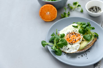 Toast (sandwich) with cream cheese, avocado, fried egg and greens on gray wooden background. Selective focus. Healthy eating or vegetarian food concept