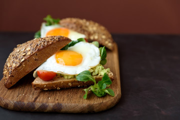 Rye sandwiches (burgers) with avocado, tomato, fried egg and greens on brown wooden background. Selective focus. Healthy eating or vegetarian food concept