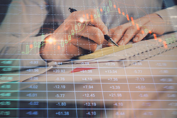 Close up of hands writing with double exposure of business charts. Financial concept.