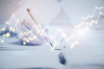 Close up of hands writing with double exposure of business charts. Financial concept.