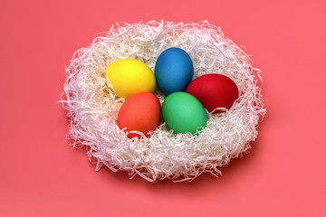 Fototapeta na wymiar Five Easter colored eggs lie in the nest in the center on a gently pink background, top view. From the nest is falling hard the shadows. Horizontal photo.