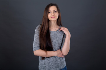 Portrait of a young brunette woman with long hair on a gray background.