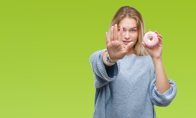Young caucasian woman eating sweet donut over isolated background with open hand doing stop sign...