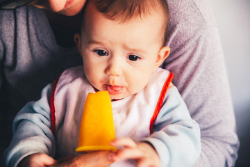 Baby smiling and drooling when trying for the first time an ice cream from his mother's hands, infant feeding through the baby led weaning method