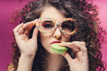 Beautiful girl eat green macaroon in confectionery dressing glasses