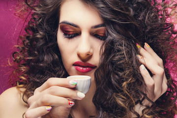 beautiful curly girl with colourful manicure drinking from a very small cup