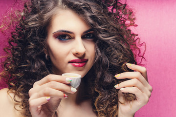 beautiful curly girl with colourful manicure drinking from a very small cup