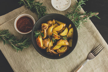 Bowl of baked potatoes with rosemary, tomato and cream sauce on rustic background.