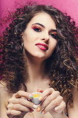 beautiful curly girl with colourful manicure smile and drink from a small cup